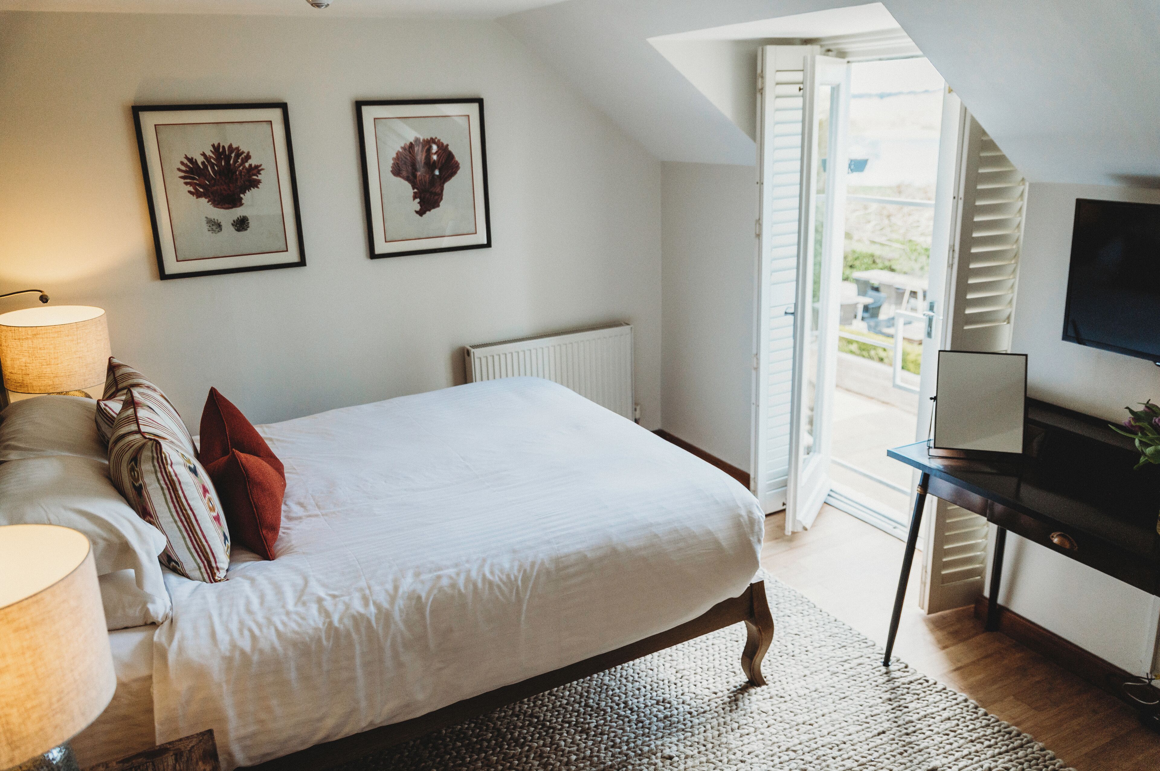 A bedroom with a bed, a bedside table, a lamp, and two framed pictures on the wall.