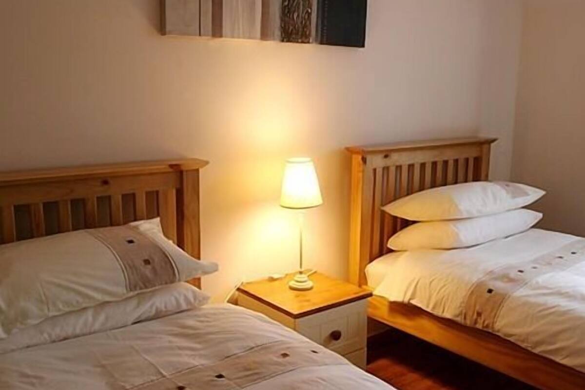 A double bed with a wooden headboard, a bedside table with a lamp, and a nightstand with a drawer.