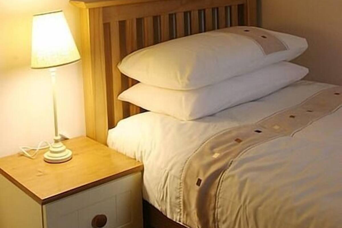 A neatly made bed with a wooden headboard, a bedside lamp, and a nightstand with a drawer.