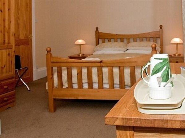 Una cama de madera con dos lámparas de noche, una mesita de noche de madera y una bandeja con una taza y una cuchara.