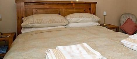 Un lit bien fait, avec une tête de lit en bois, deux oreillers et une couverture pliée posée sur le lit.