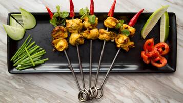 Un plato rectangular negro con brochetas de pollo a la parrilla, rodajas de pepino, cebolletas, chiles rojos y gajos de lima.