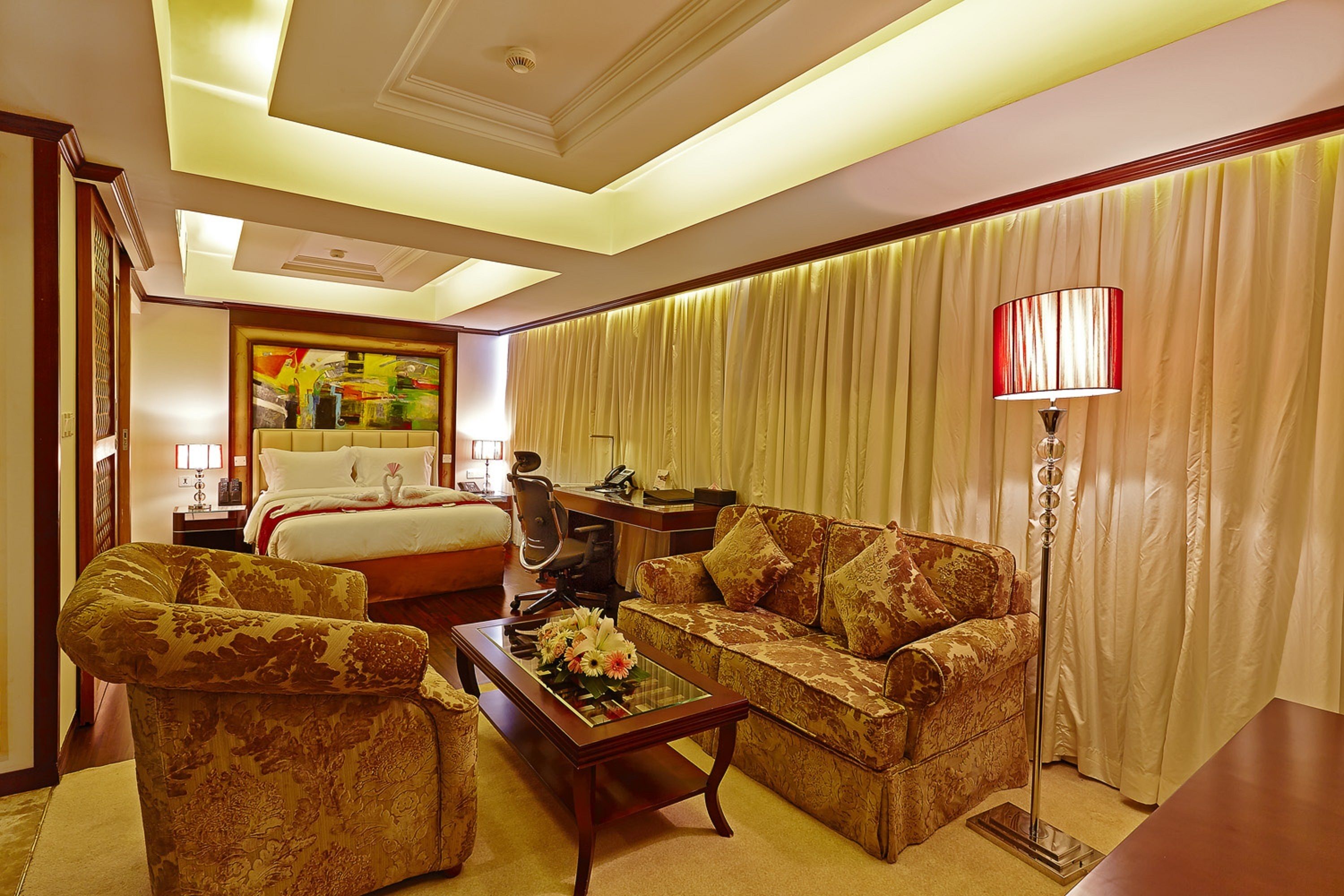 A hotel room with a bed, two sofas, a coffee table, a desk, and a lamp.