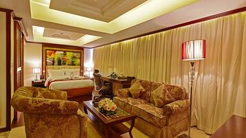 A hotel room with a bed, two sofas, a coffee table, a desk, and a lamp.