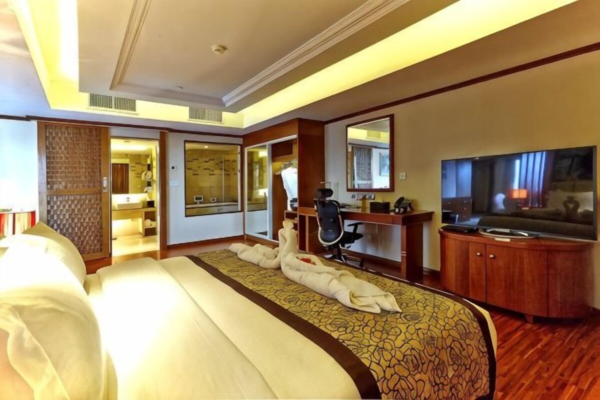 A hotel room with a bed, a desk, a television, and a bathroom visible through an open door.