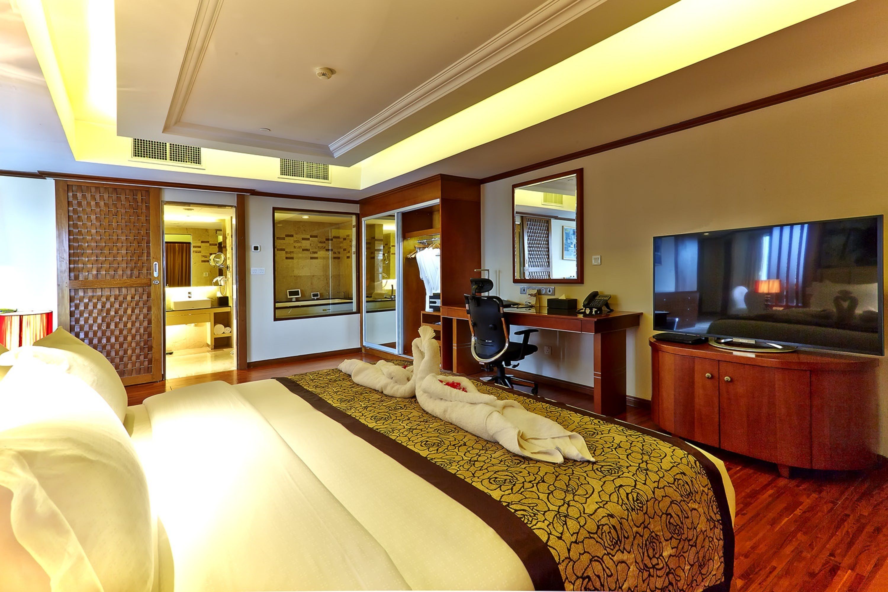 Habitación de hotel con una cama grande, un escritorio con silla, un televisor y un espejo.