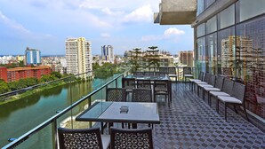 A balcony with tables and chairs overlooking a river and cityscape. - Six Seasons Hotel (Dhaka)
