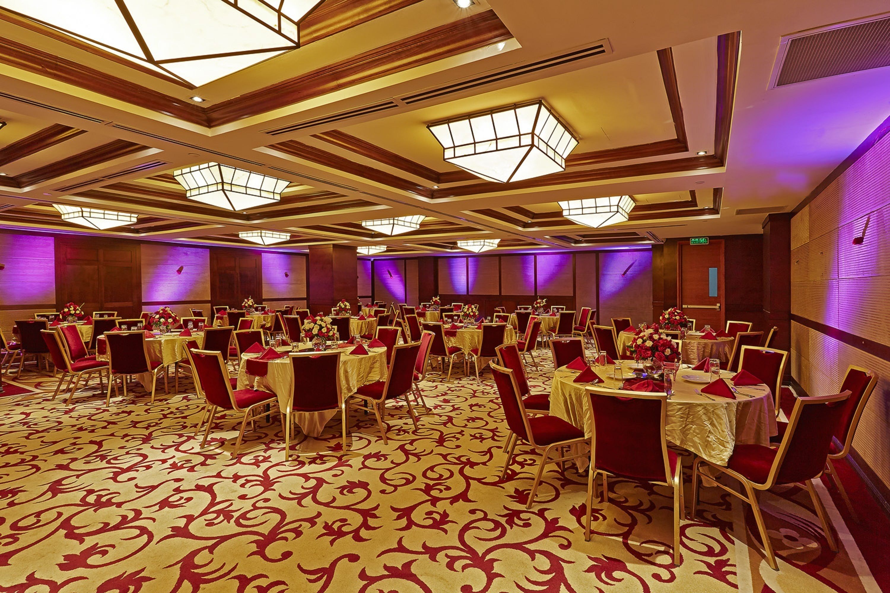 Un salón de banquetes con mesas redondas, sillas rojas y una alfombra estampada.