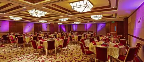 Un salón de banquetes con mesas redondas, sillas rojas y una alfombra estampada.
