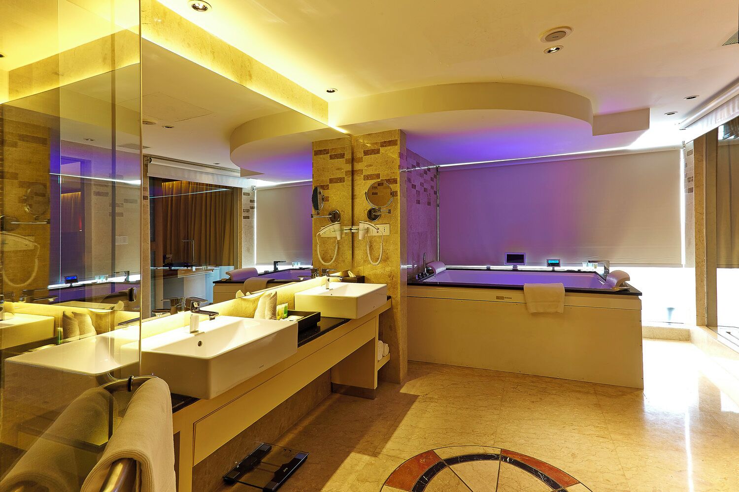 A modern bathroom with dual sinks, a large mirror, a bathtub, and a vanity with a towel rack.