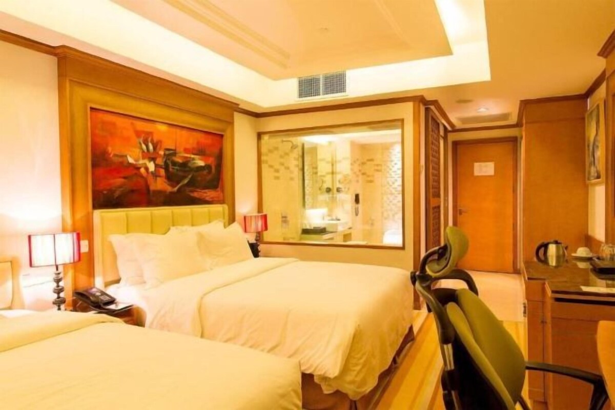 A hotel room with two beds, a large mirror, a desk, and a painting on the wall.