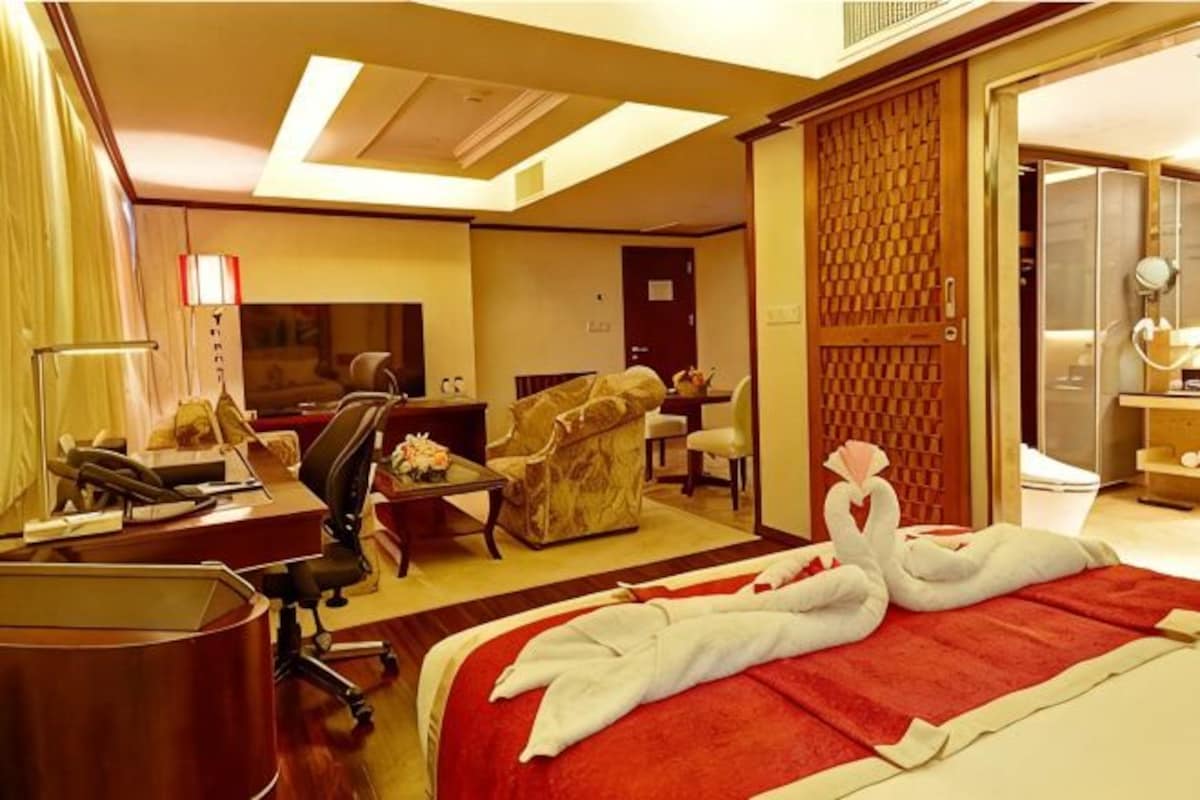 A hotel room with a bed, a desk, a chair, a sofa, and a TV.