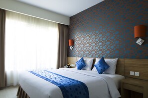 Une chambre d’hôtel avec un grand lit, deux oreillers, une table de chevet, une lampe et un mur décoré d’un motif.