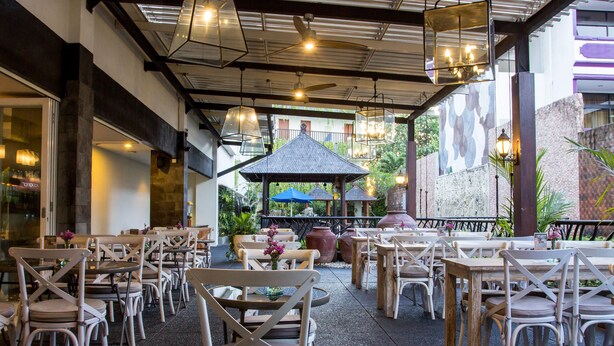 An outdoor dining area with wooden tables and chairs, a gazebo, and hanging lights.