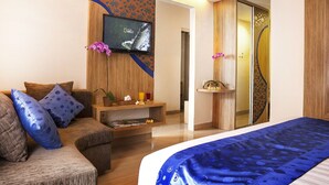 A hotel room with a bed, a sofa, a TV mounted on the wall, a small table with a plant, and a sliding door with a decorative panel.