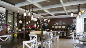 A spacious dining area with white chairs and tables, decorative wall art, and hanging pendant lights.