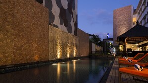 A pool area with stone walls and a modern design, including a lounge area with orange seating.