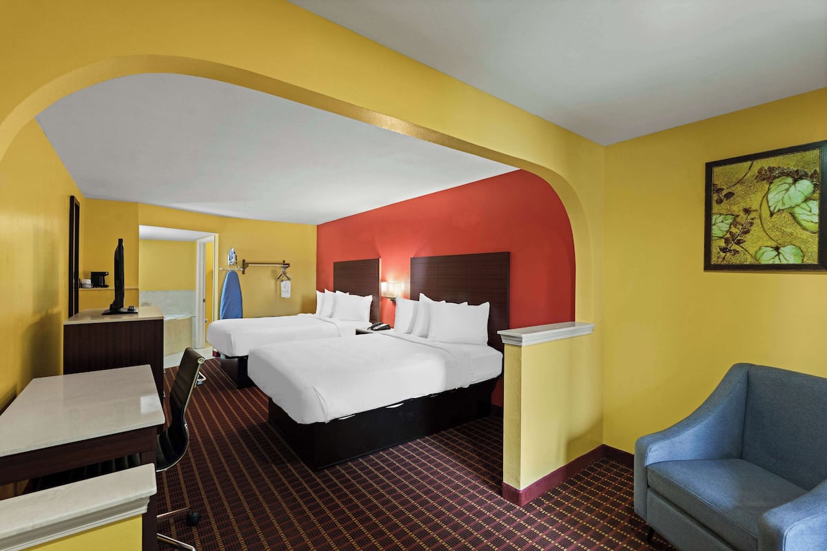 A hotel room with two beds, a desk, a chair, and a painting on the wall.