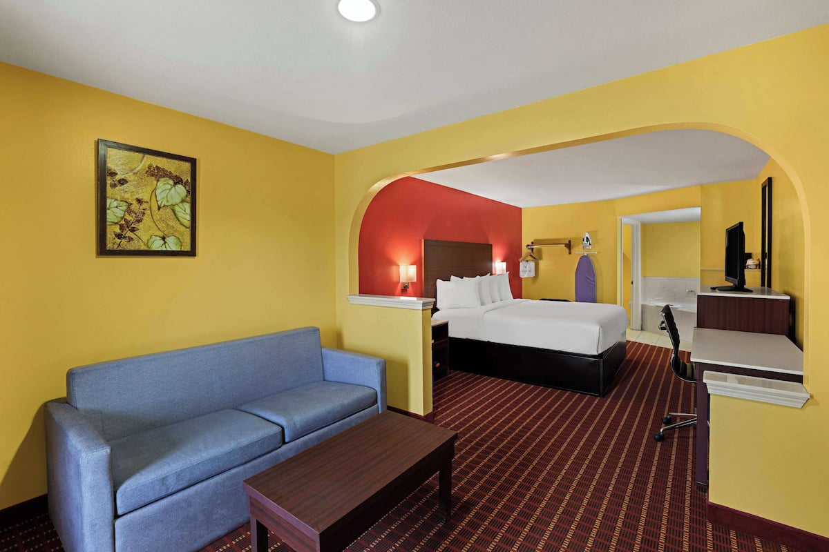A hotel room with a bed, a sofa, a desk, and a bathroom visible through an archway.
