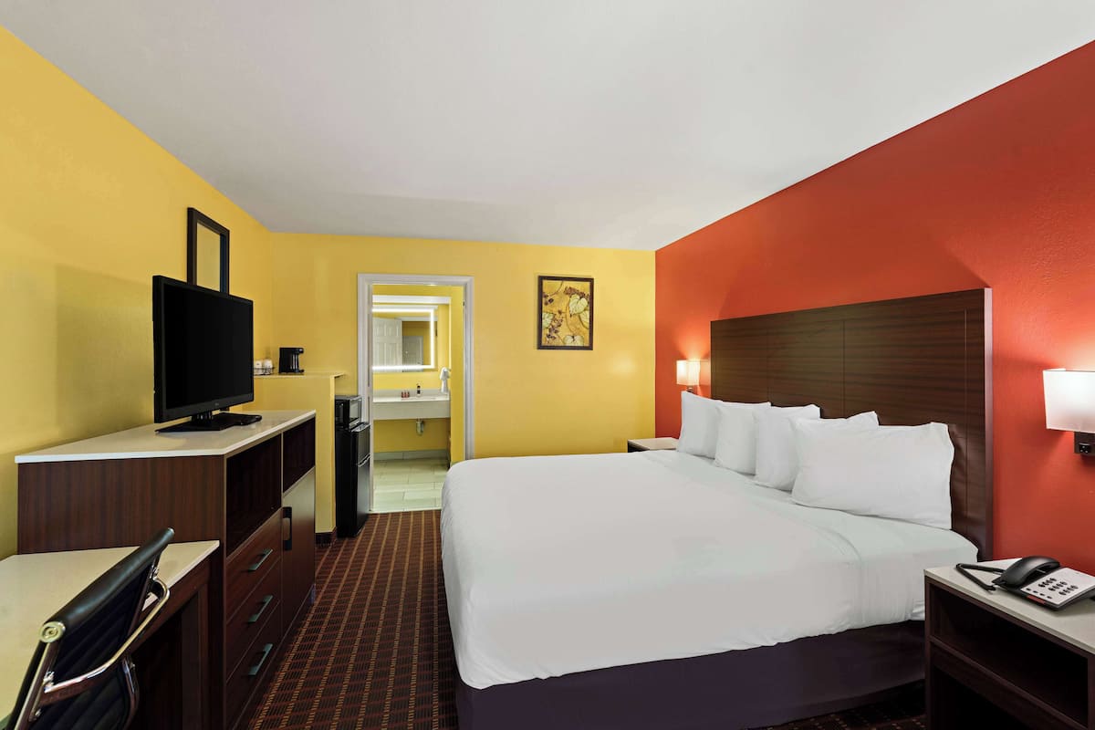 A hotel room with a bed, a desk, a television, a telephone, and a bathroom visible through an open door.