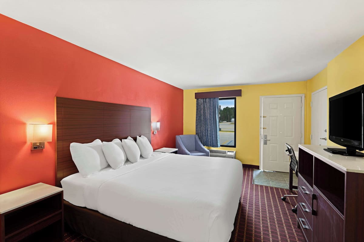 A hotel room with a large bed, a desk, a chair, a television, and a window with curtains.