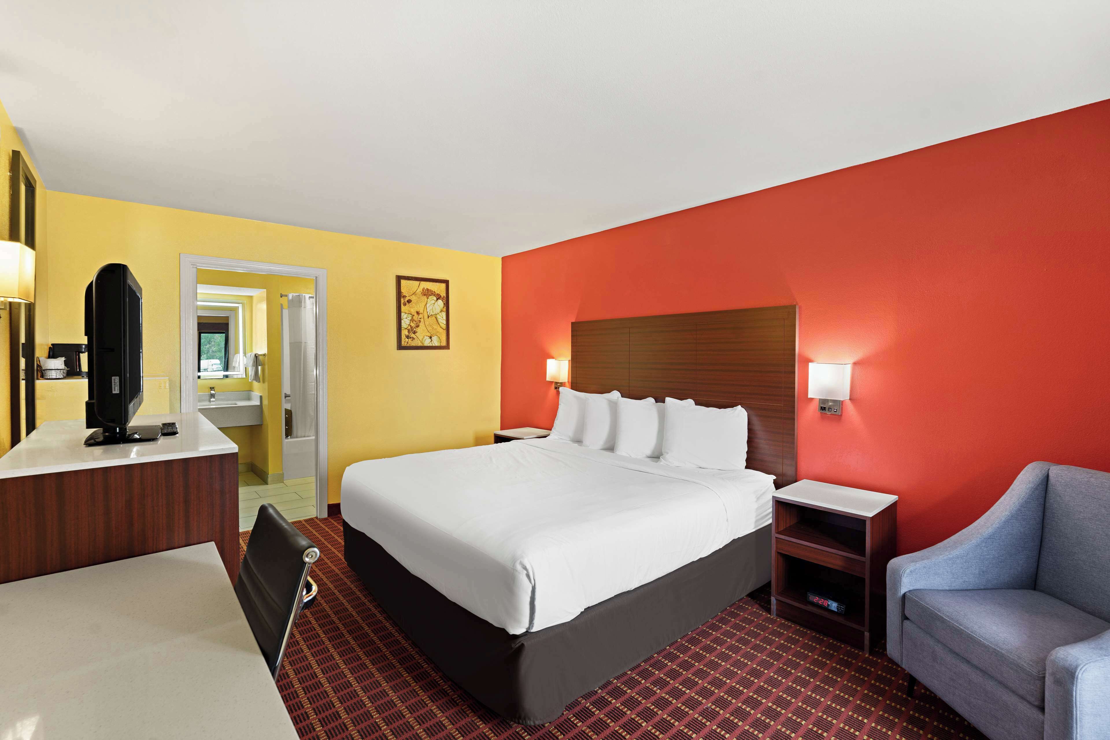 A hotel room with a bed, a desk, a chair, a nightstand, and a TV.