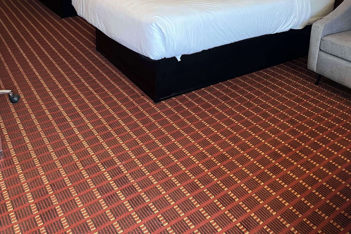 A hotel room with two beds, a red carpet, and a yellow wall.
