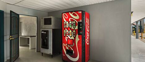 A Coca-Cola vending machine in a hallway with a door and an air conditioning unit.