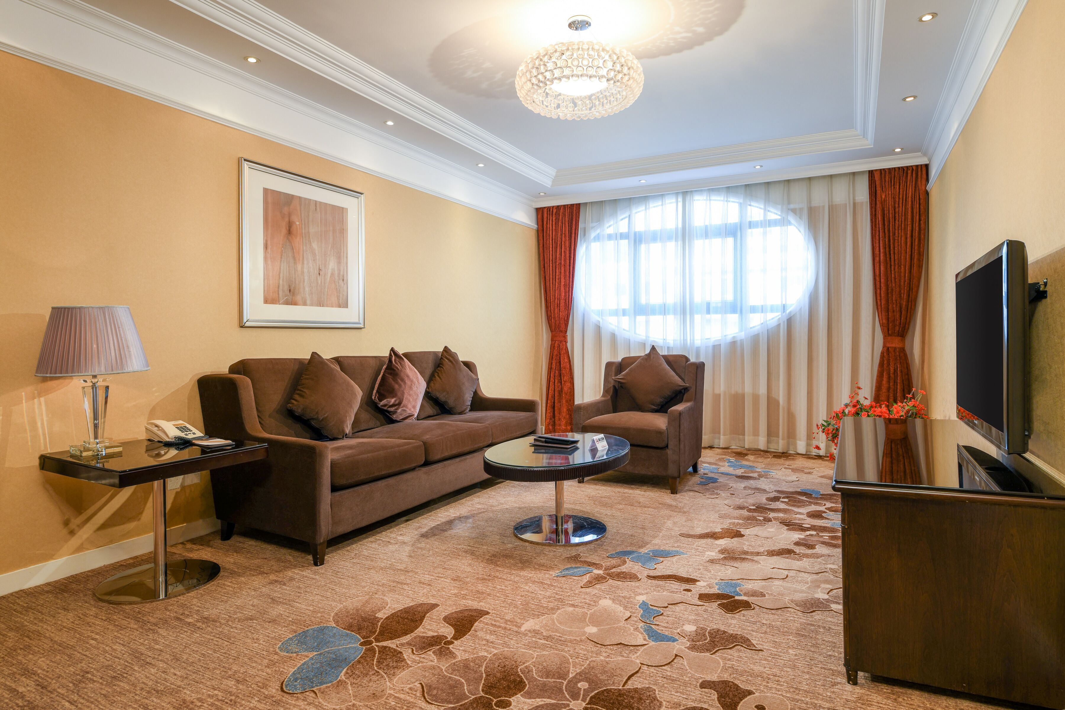 A hotel room with a brown sofa, a round coffee table, a TV, and a patterned carpet.