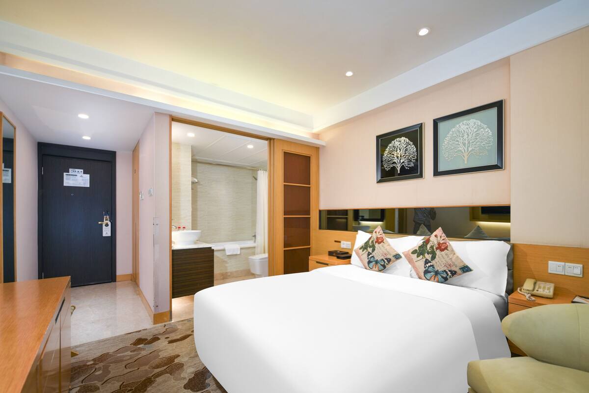 Una habitación de hotel con una cama, mesita de noche y baño visible a través de una puerta abierta.