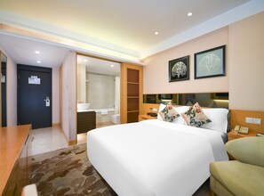 Een hotelkamer met een bed, nachtkastje en een badkamer zichtbaar door een open deur.