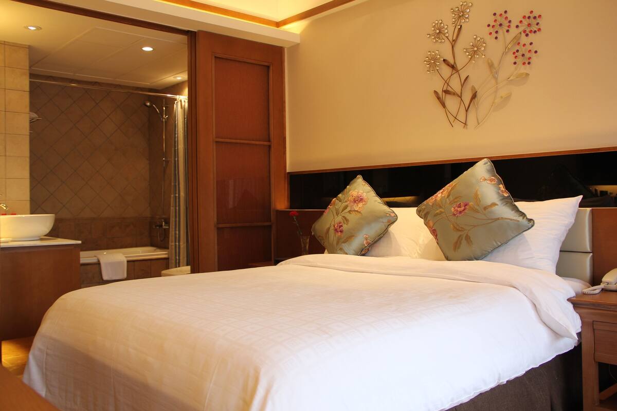 Una habitación de hotel con una cama grande, una mesita de noche, un baño con ducha y un adorno en la pared.