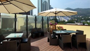 A rooftop terrace with wicker furniture, large umbrellas, and a view of a tall building and surrounding landscape. - Honlux Apartment (Shenzhen)