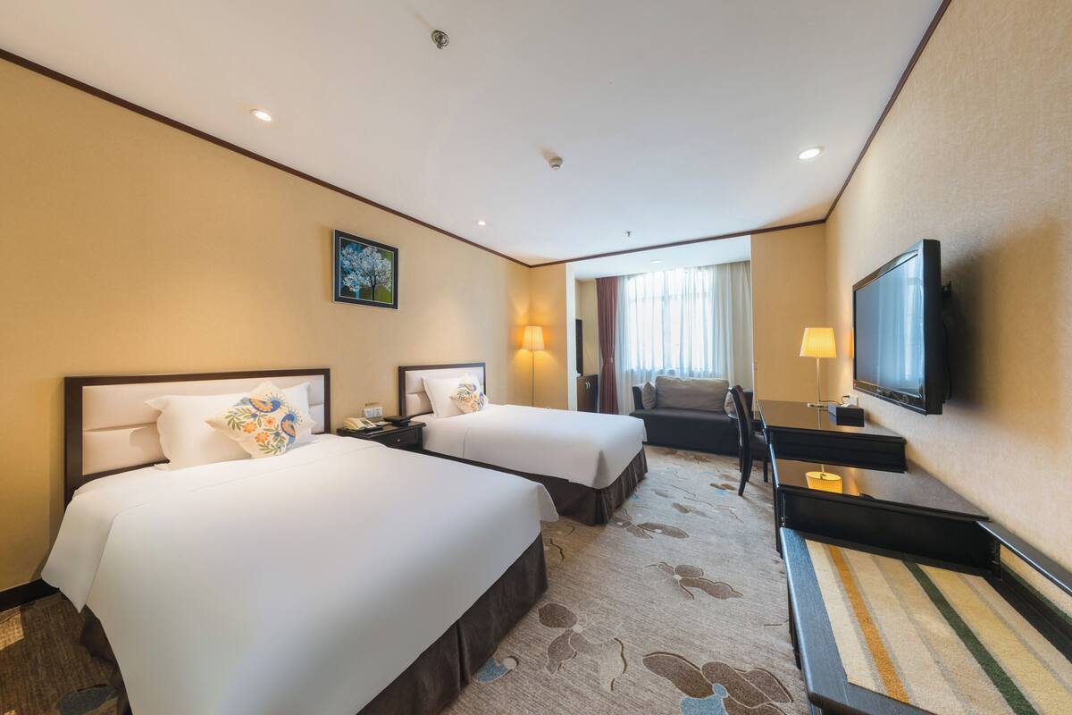 Habitación de hotel con dos camas, un escritorio, un televisor y un sofá.