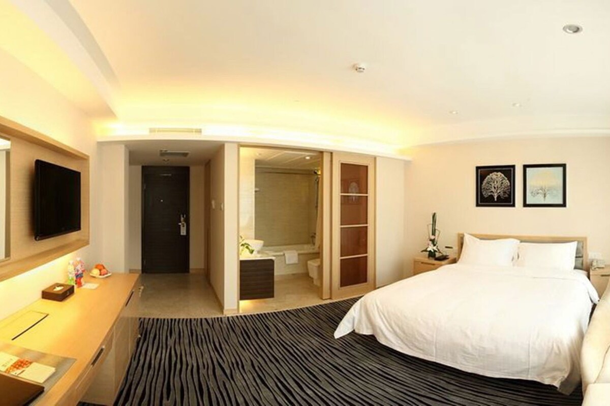 A hotel room with a bed, a desk, a mirror, a bathroom, and a wardrobe.