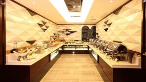 A modern hotel lobby with a geometric patterned wall, a central reception desk, and a buffet area with various food items. - Honlux Apartment (Shenzhen)