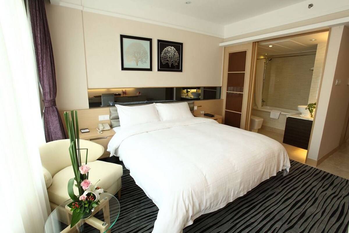 A hotel room with a large bed, a desk, a chair, a mirror, and a wardrobe.