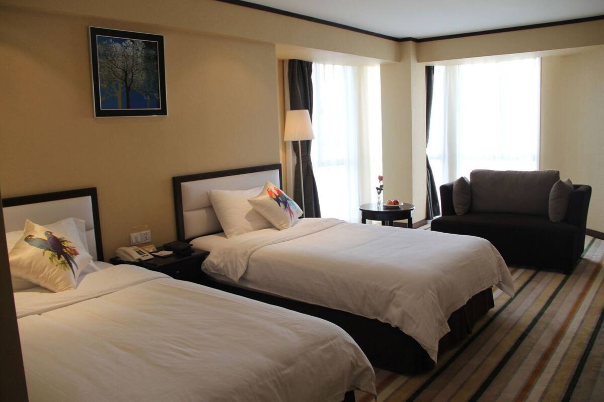 A hotel room with two beds, a sofa, a lamp, and a painting on the wall.