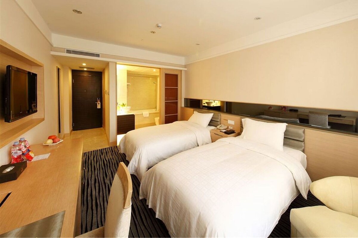 A hotel room with two beds, a desk, a TV, a bathroom, and a minibar.