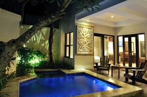Zona de piscina con borde de azulejos, rodeada de follaje y un muro decorativo.