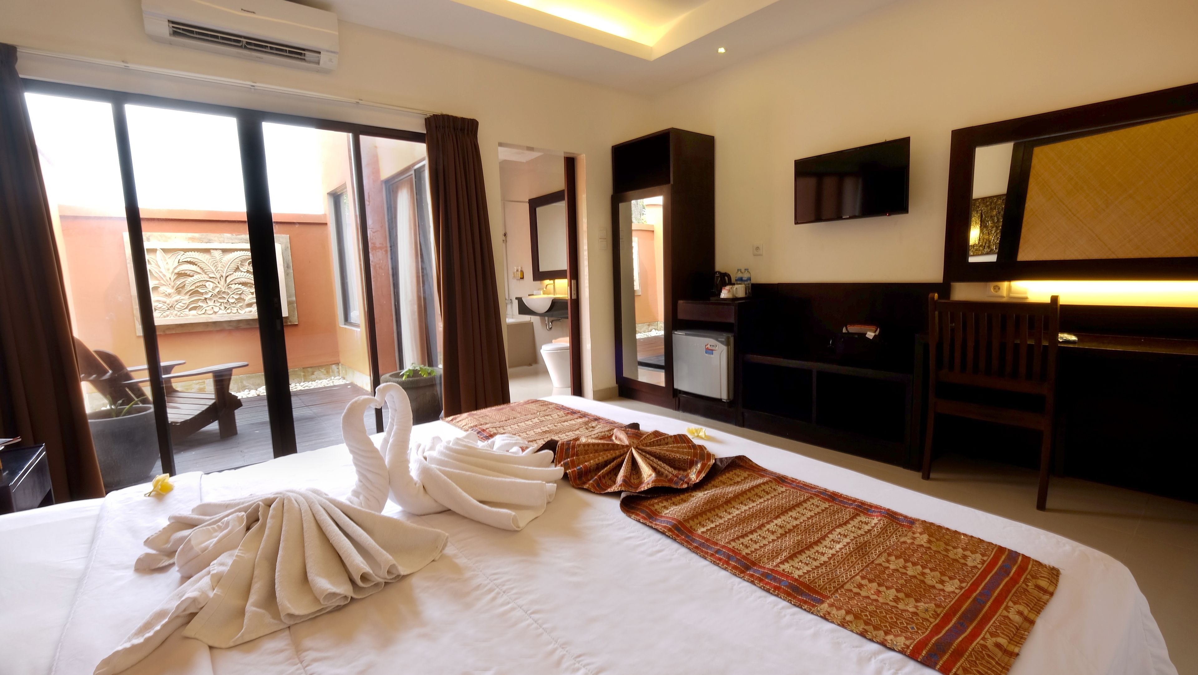 Habitación de hotel con una cama grande, un escritorio, una silla, un televisor y un balcón con vistas al exterior.