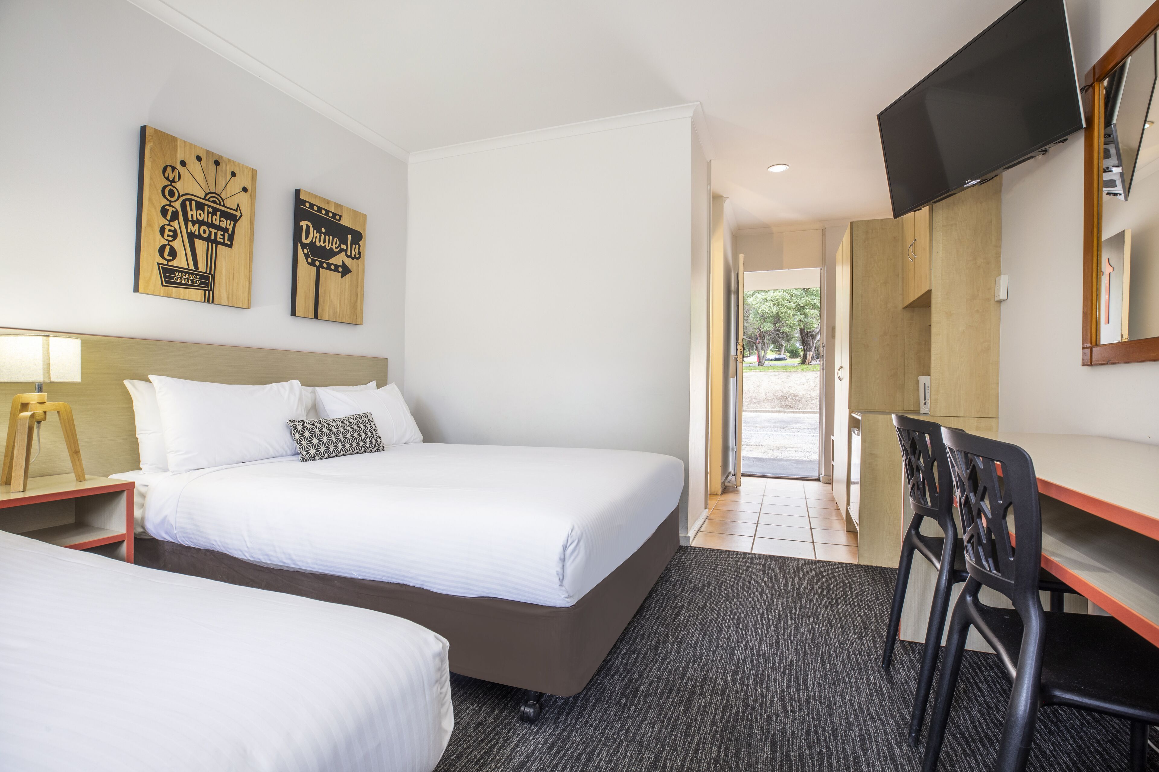 Una habitación de hotel con dos camas, un escritorio con silla, televisor y decoración en la pared.