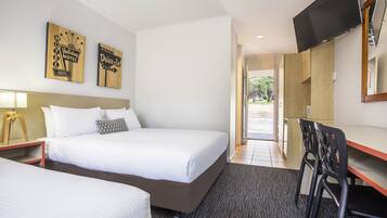Una habitación de hotel con dos camas, un escritorio con silla, televisor y decoración en la pared.