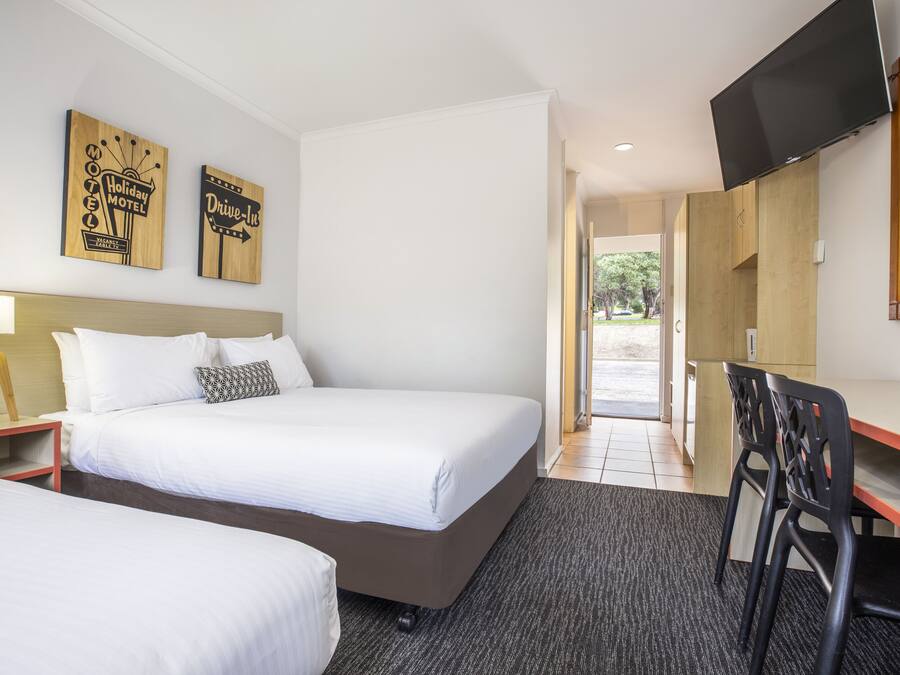 Una habitación de hotel con dos camas, un escritorio con silla, televisor y decoración en la pared.