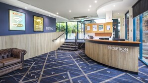 A reception area with a reception desk, a couch, and a staircase leading to an upper level. - Burvale Hotel (Vermont South)