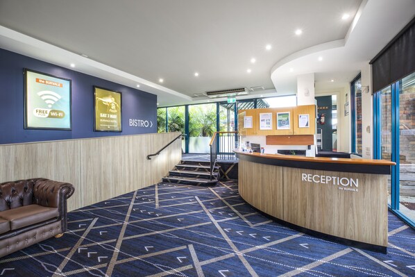 A reception area with a reception desk, a couch, and a staircase leading to an upper level. - Burvale Hotel (Vermont South)