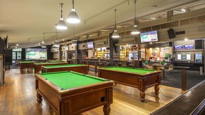 A pool hall with multiple pool tables, overhead lighting, and a bar area with a television screen. - Burvale Hotel (Vermont South)