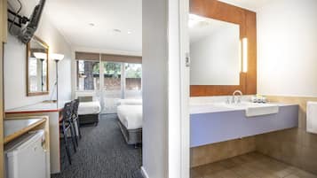 Habitación de hotel con cama, escritorio, silla, refrigerador, espejo grande y baño con lavamanos e inodoro.