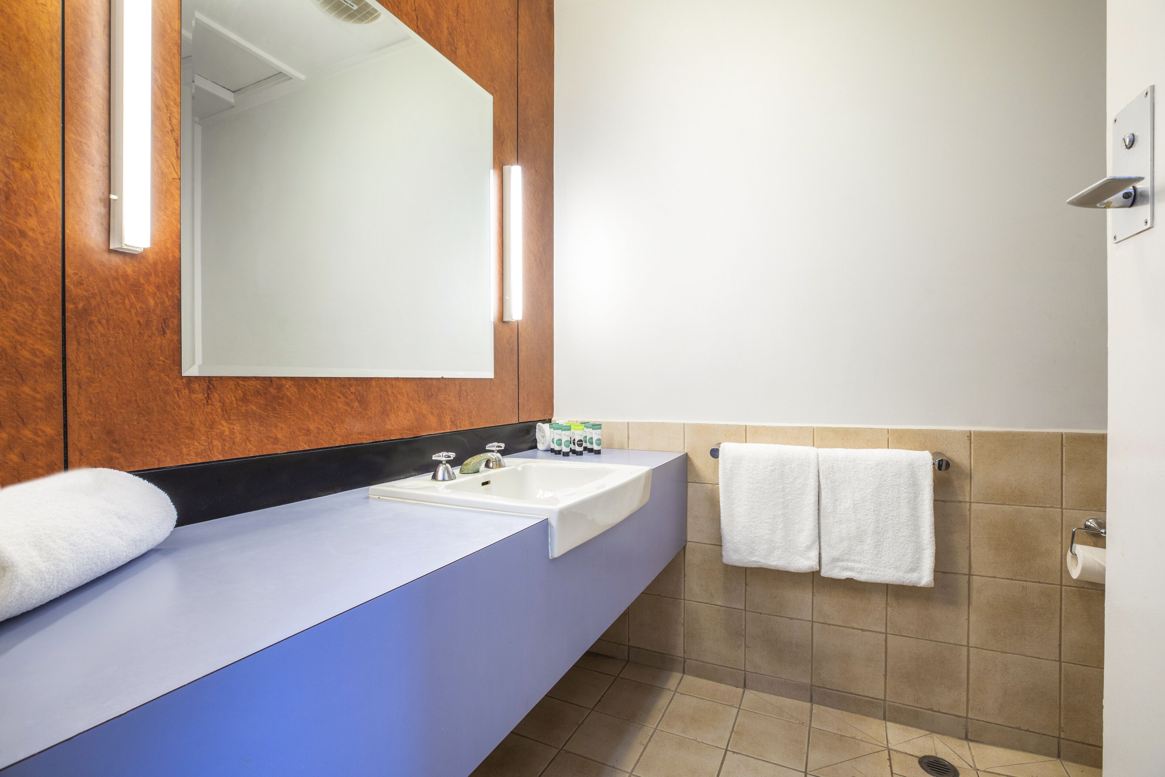 A bathroom with a wooden vanity, two sinks, a mirror, and a towel rack.