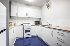 A kitchen with white cabinets, a microwave, an oven, and a sink. - Burvale Hotel (Vermont South)